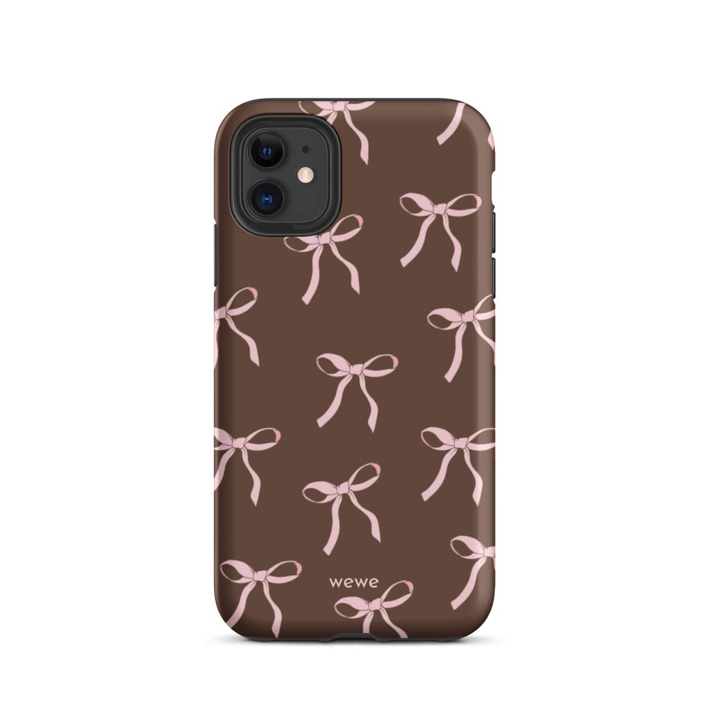 Custom iPhone 11 tough case in matte dark brown (chocolate) featuring an all-over repeating pattern of light pink ribbons/bows, with 'wewe' branding at the bottom.