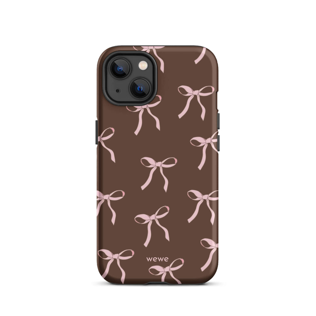 Custom iPhone 13 tough case in matte dark brown (chocolate) featuring an all-over repeating pattern of light pink ribbons/bows, with 'wewe' branding at the bottom.